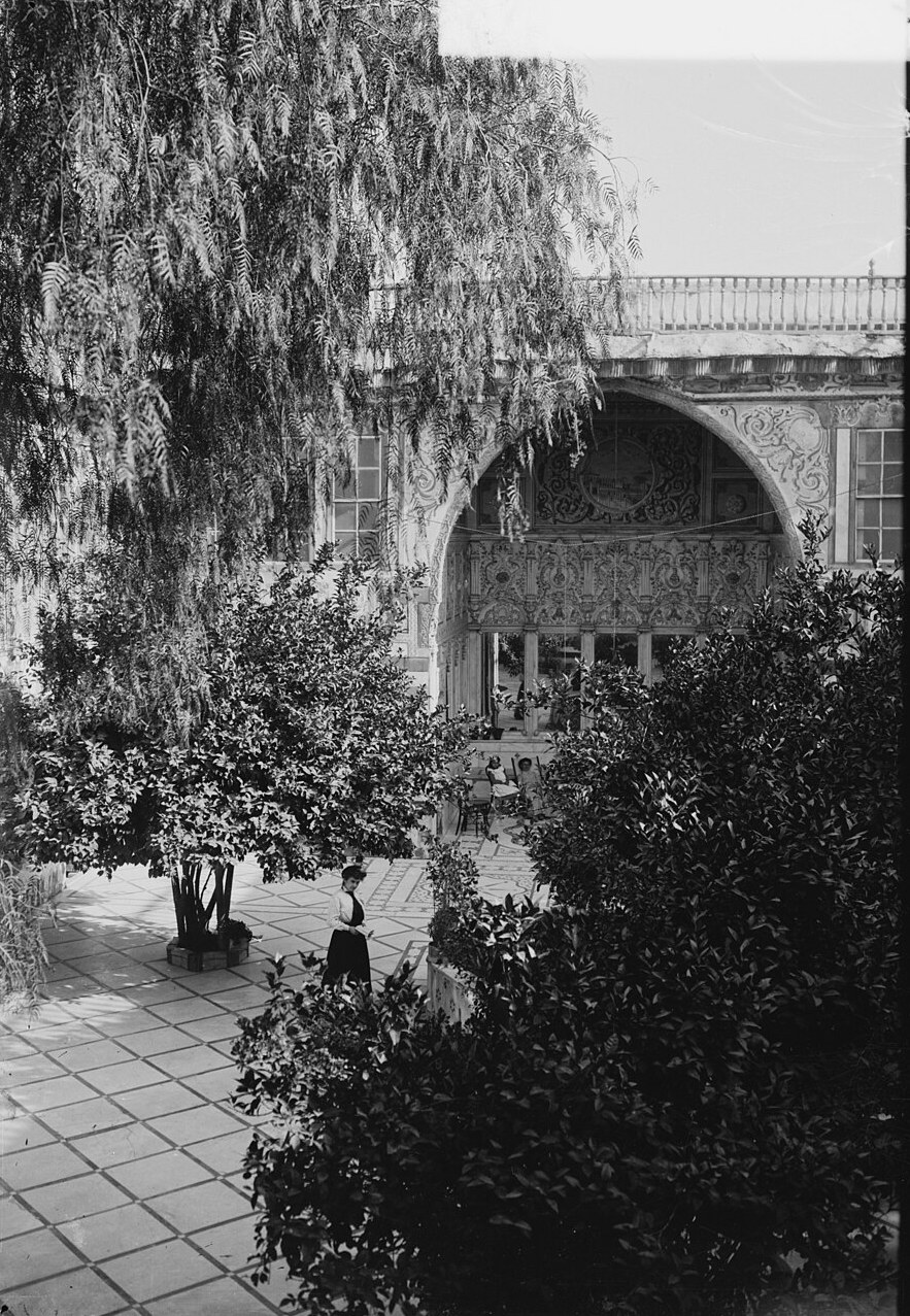 Historic black-and-white photograph of a Damascus courtyard house with an arched iwan and citrus trees.
